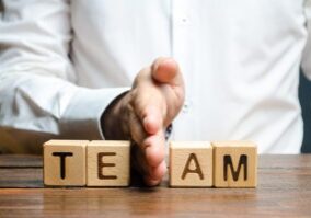 A Man Shares With His Hand Cubes With The Inscription Team. Dividing The Collective Into Two Parts Or Disbanding The Team. Lack Of Leadership Qualities And Poor Quality Of Business Management.